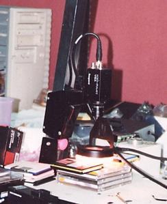 縦に伸びる黒い金属製のレールに、カメラが取り付けられている。被写体のすぐ上に置いてあるルーペ状の装置が検査部にあたる