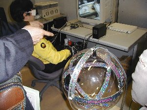 こちらは3次元ゴーグルとマニピュレーター操作用のグローブだけで構成されるミニマムコックピット。手前の球体はグローブの位置を検出するための磁気を放射するもの 