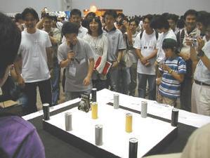 テーブル上の空き缶を下に落とす時間を競うミニ競技。組み上げるロボットの機能やプログラミングで差がつく。多くの観客が集まった  