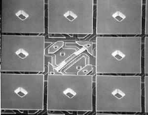 DMDの表面の電子顕微鏡写真。真中にへこみのある四角1つ1つがマイクロミラーで、1辺の長さは16μm、ミラー同士の間隔は1μmで整然と並んでいる。最下層のシリコンウェハー上の部分の製造工程は、SRAMのものとほぼ同じなのだという (c)Texas Instruments