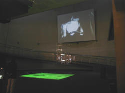 南青山のスパイラルガーデンで開催中の第4回プロスペクト展“DRIVE”。床に映る緑色の映像は、湾岸戦争などの空撮映像を編集しているらしい