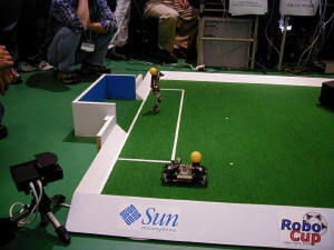 4脚ロボットはフォワード。ボールをゆっくりと追いかけていく。2足ロボットはキーパーだったが……。手前の4輪操舵の高速ロボットはフルスピードだとフィールドを飛び出てしまうので、性能を抑えての参加だ 
