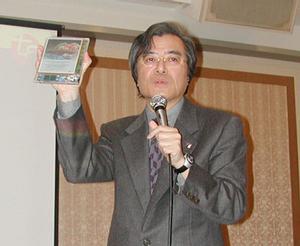 発表会でT-Engineについて説明する、TRONプロジェクトの坂村健教授。手に持っているのは電子書籍端末のモックアップ