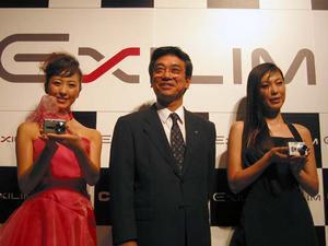 常務取締役の鈴木洋三氏が、左には『EX-S100』を、右には『EX-Z55』を手にしたコンパニオンを並べてフォトセッションを実施