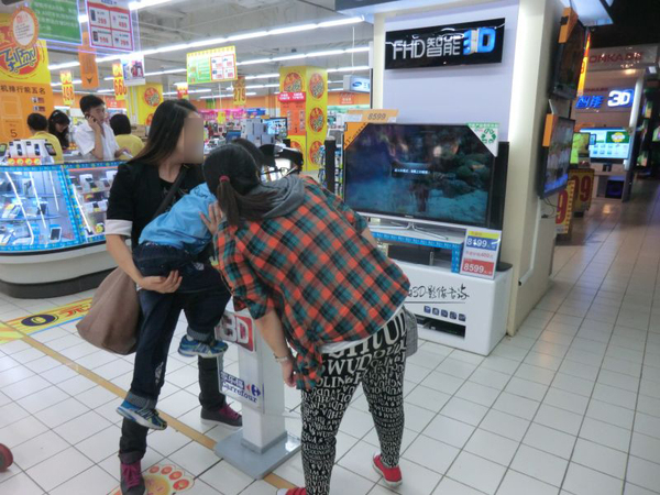 スーパーのテレビ売場で3Dテレビを見る家族連れ