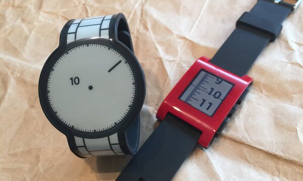 同じような電子ペーパーを採用している先輩格の「Pebble腕時計」（右）。Pebbleのベルトは単なるラバー製だが、充電式でスマホと連携し、文字盤の時刻は常時表示だ